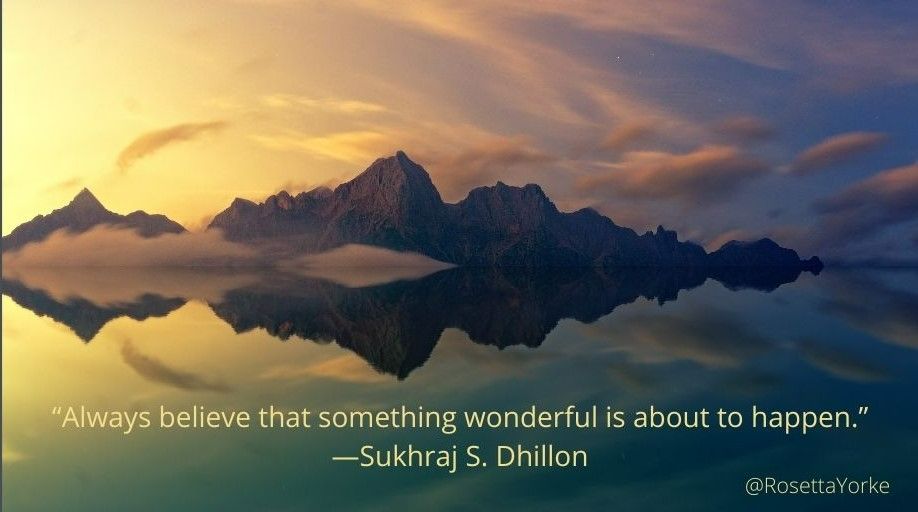 Yellow-gold dawn breaking through from the left of an indigo sky, illuminating jagged mountain peaks overlooking a tranquil lake.