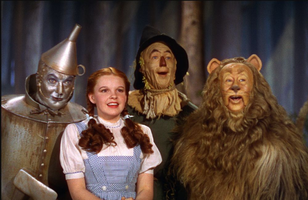 The Tin Man, Dorothy, Scarecrow, and Lion smiling in The Wizard of Oz