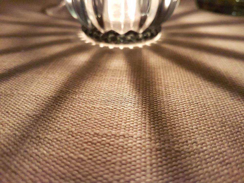 Ein geriffeltes Glas auf einem beigen, gewebten Stoff, die Schatten der Riffel strahlen sternförmig 