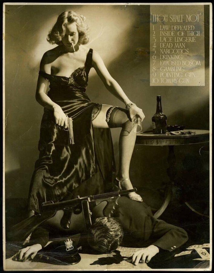 A blonde bombshell in a black negligee with bare shoulders and arm and a deep neckline is standing with one leg exposed on a gangster in a dark suit who is lying dead on his stomach. She wears black sexy stockings and holds a gun in her hand. She is pointing it at the dead guy who has a big black machine gun next to him. You can see blood seeping from his head, a police hat and playing cards around him. She is also smoking with a cigarette between her lips and an empty glas in the other hand. In the background is a dark bottle with alcohol on a table and a syringe. 
In the upper right corner are the rules that picture violated: Thou shall not... 1. Law Defeated, 2. Inside of thigh, 3. Lace Lingerie, 4. Dead Man, 5. Narcotics, 6. Drinking, 7. Exposed Bosom, 8. Gambling, 9. Pointing Gun, 10. Tommy Gun.
