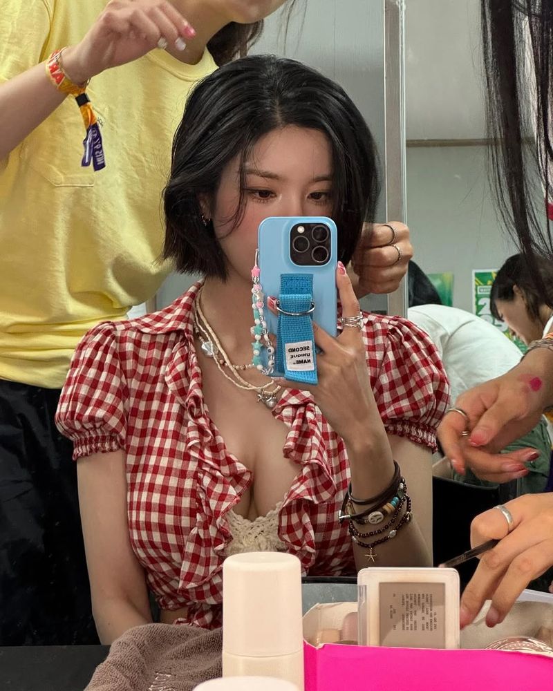 Eunbi in a checked red and white shirt and white top, getting her hair and makeup done