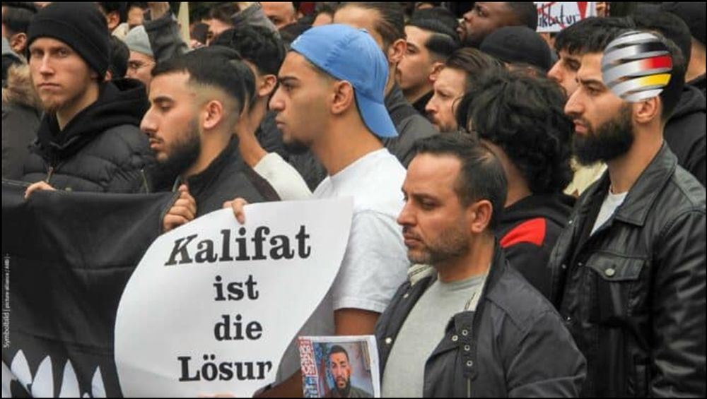 Auf dem Foto sind fast ausschließlich ausländisch aussehende Männer auf einer Demonstration zu sehen und sie tragen ein Banner mit der Aufschrift: „Kalifat ist die Lösung“.