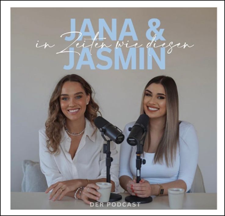 Ein Foto vom Podcast Jana & Jasmin "in Zeiten wie diesen". Beide haben vor sich einen Becher mit vermutlich Kaffee, jede hat ein Mikrofon. Sie tragen weiße Kleidung und ihre Zähne sind schwanenweiß.