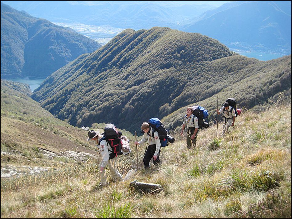 Mehrere Jugendliche auf einer Wanderung in den Bergen. Sie tragen gefüllte Rucksäcke und Wanderstäbe.