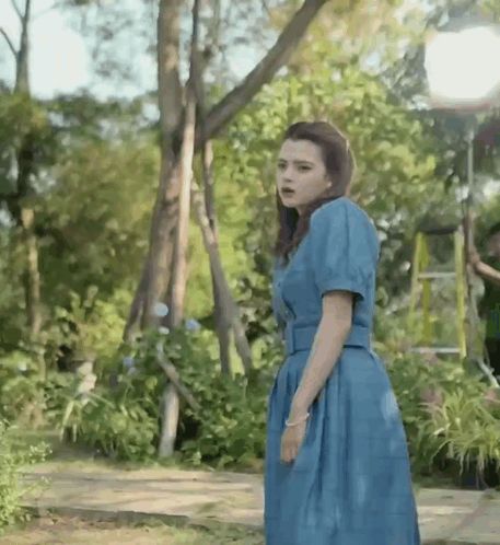 a woman in a blue dress is standing in a forest