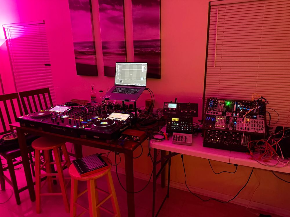 living room setup with a pair of CDJs, mixer, Ableton on laptop, MIDI controllers, and some synth equipment 