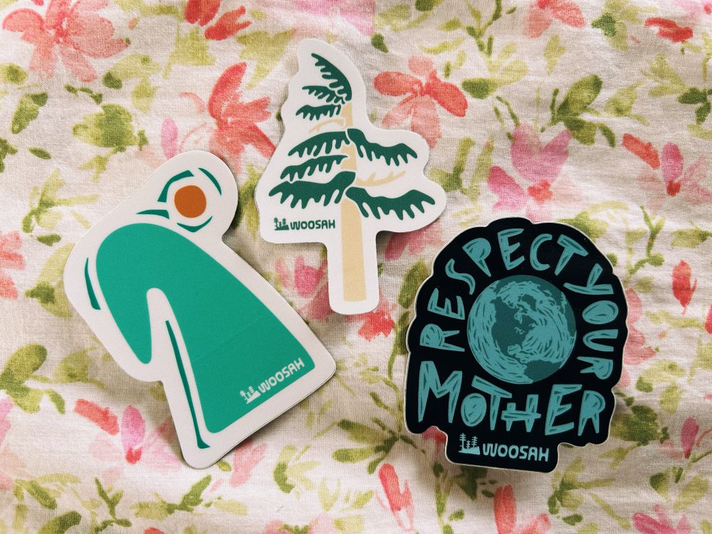 3 stickers on floral bedding: an abstract wave with a sun, a cedar tree, and a sticker of planet earth with the words “respect your mother”