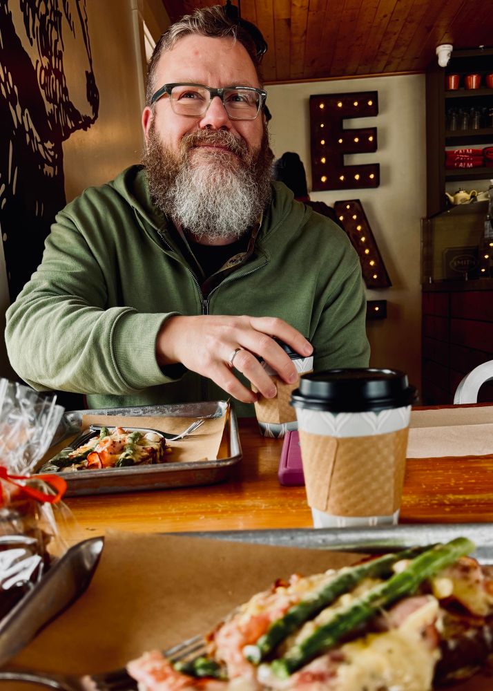 Bearish man reaching for a coffee with croque monsieur in the foreground. 
