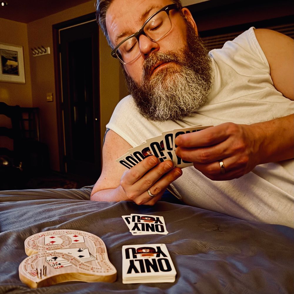 Bearish man playing cribbage with Smokey the Bear playing cards. 