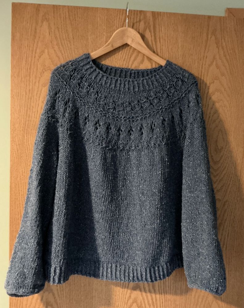 Denim blue colored sweater hanging on a hanger in front of wooden door.