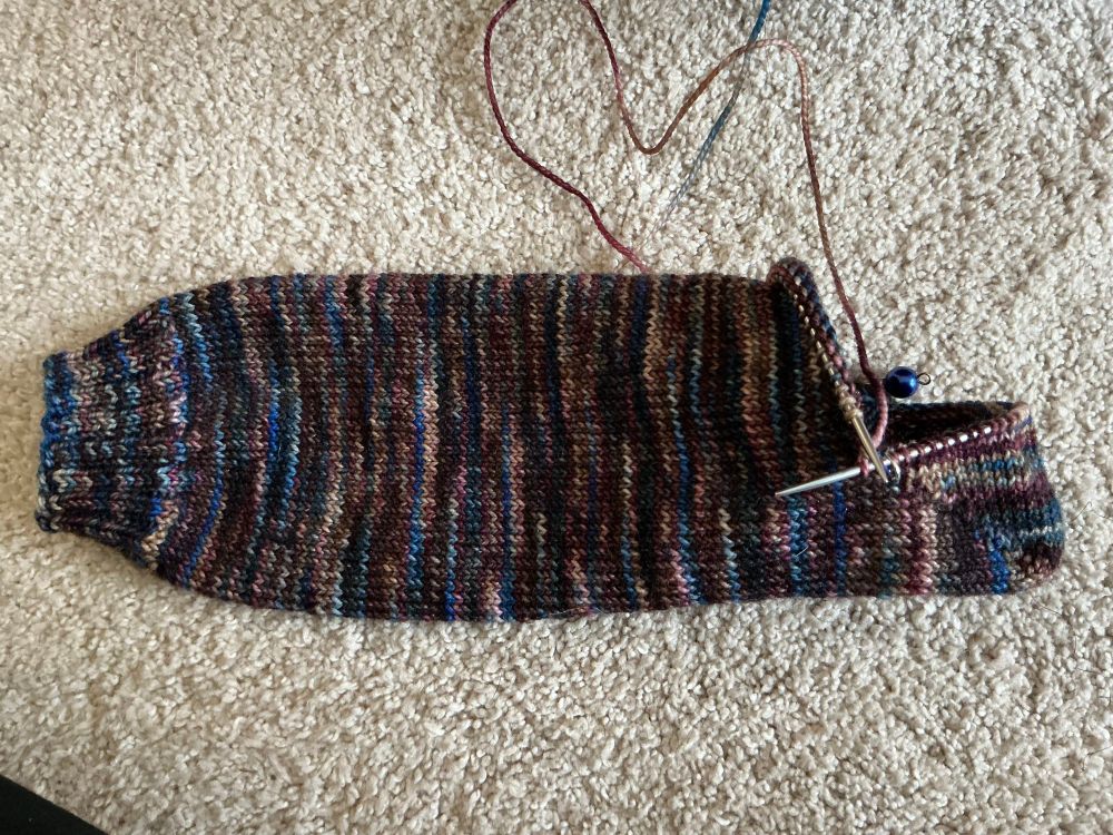 Partially knit sock lying on beige carpet