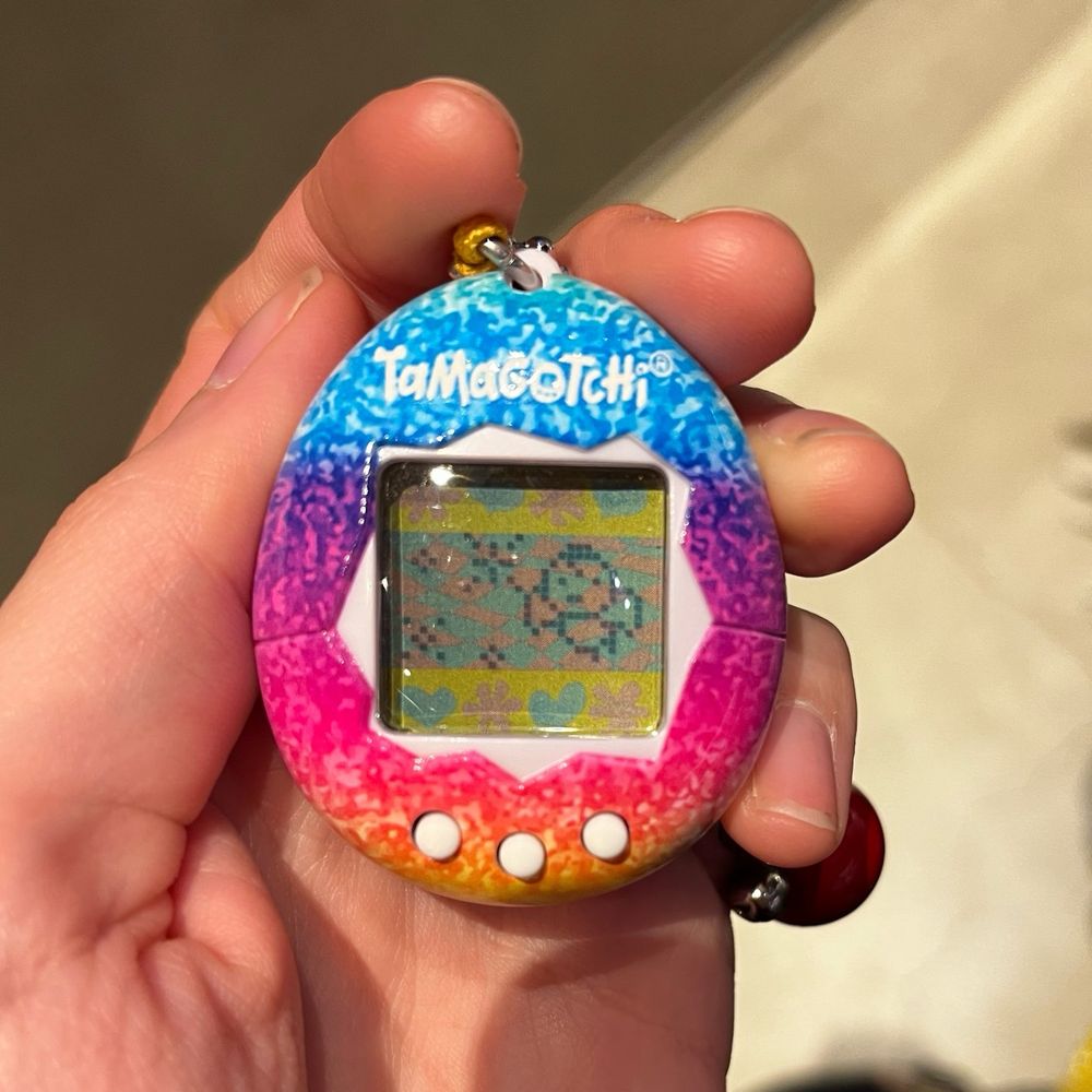 Picture of hand holding a tamagotchi with on the screen an angel. 