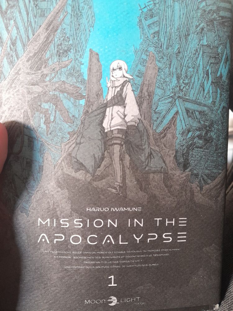 Couverture du manga "Mission I the apocalipse" en noir et blanc, une jeune femme en habits divers se tient sur une pile de débit dans une ville en ruine, une sac mortuaire sous le bras.
Les immeubles délabrée en fond ainsi que le ciel sont bleu-gris, seule touche de couleur.