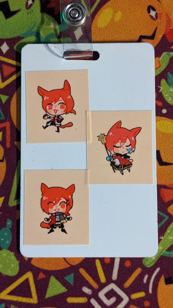 A white NFC badge with three small stickers on it featuring G'raha as he appeared in A Real Reborn, the Crystal Exarch, and G'raha in his current design all drawn in a cute chibi style.