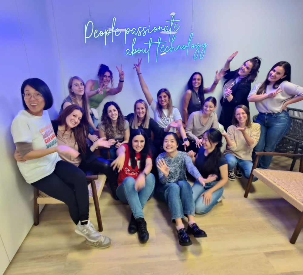 Foto de grupo de participantes de Tech SHEssions posando en una sala de ERNI, con un neón en la pared trasera que dice "People passionate about technology".
