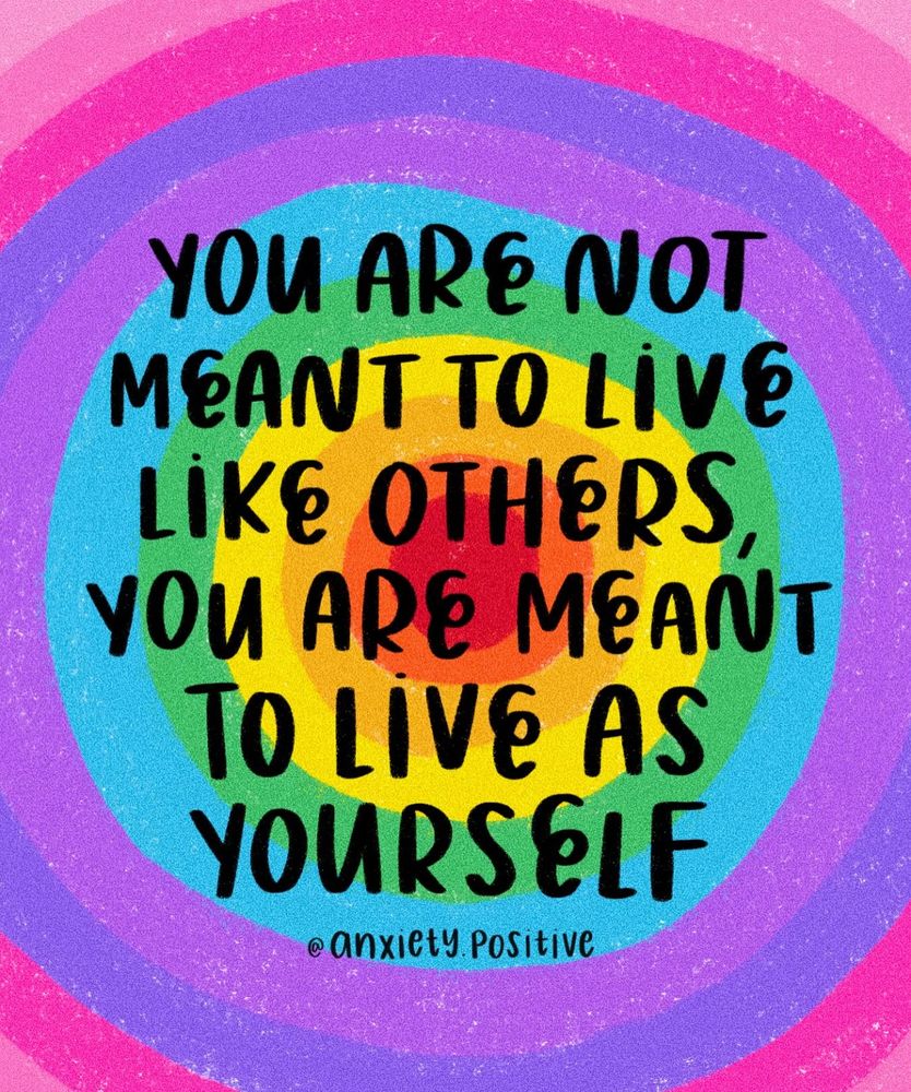 An illustration featuring concentric rainbow-coloured rings, starting with red at the centre and expanding outward through orange, yellow, green, turquoise, blue, purple, and pink. In the centre, over the red and yellow rings, bold black hand-lettered text reads: “YOU ARE NOT MEANT TO LIVE LIKE OTHERS, YOU ARE MEANT TO LIVE AS YOURSELF.” The artist’s credit, “@Anxiety.Positive”, appears in smaller text at the bottom, across the light blue and purple rings. The overall style is textured, with a crayon-like or pastel finish.