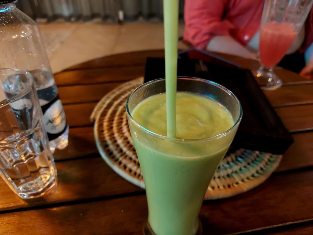 glas med trögflytande giftgrön avokadosörja och sugrör på ett bord 