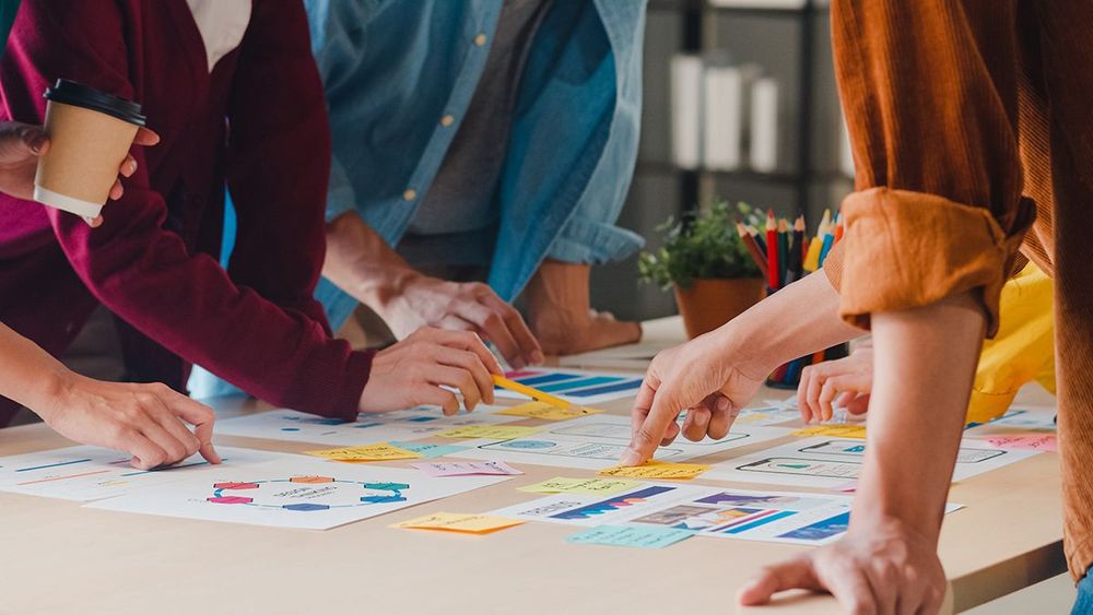 People stoo around a table looking at documents.