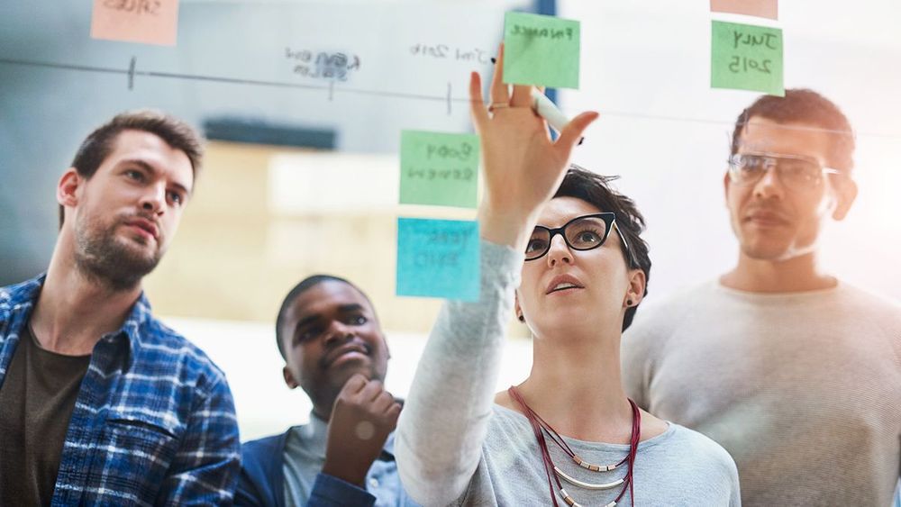 A group of people writing on post-it notes and sticking them onto a glass office wall.