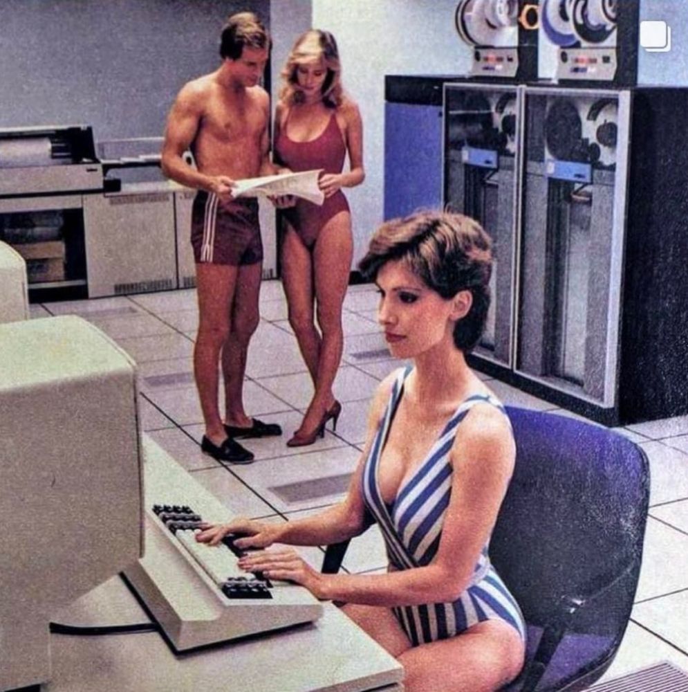vintage magazine photo of a woman in a swimsuit sitting at a computer terminal in a whole-ass mainframe room. behind her in the background, another woman in a swimsuit & high heels is going over a stack of printout with a man in trunks & loafers.
