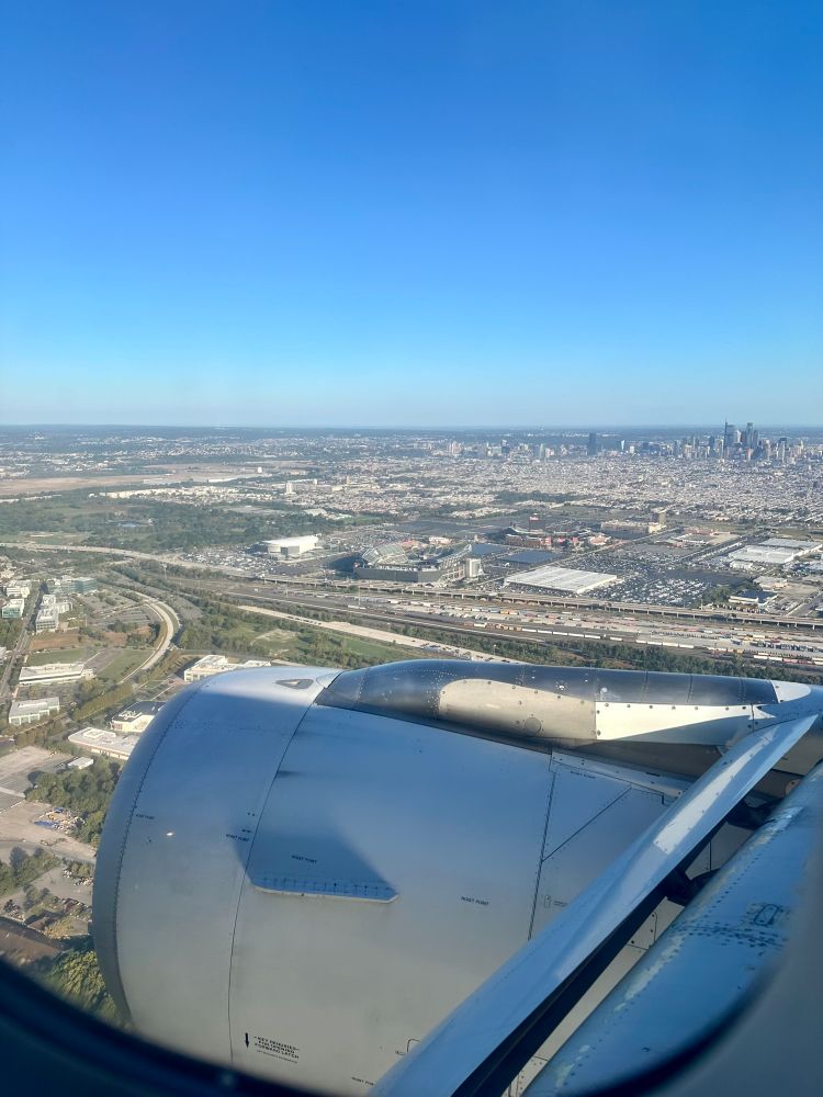 view from a plane window of the Philly skyline in the background with the eagles stadium in the front. not a cloud in the sky 