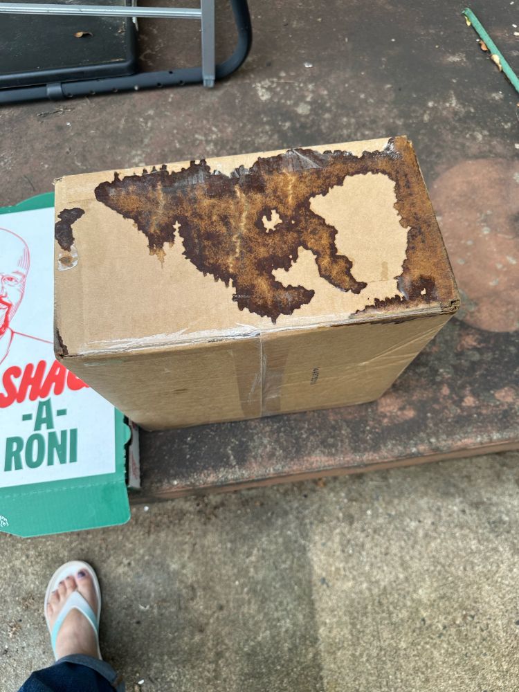 A brown cardboard box, stained and wet on its side. 