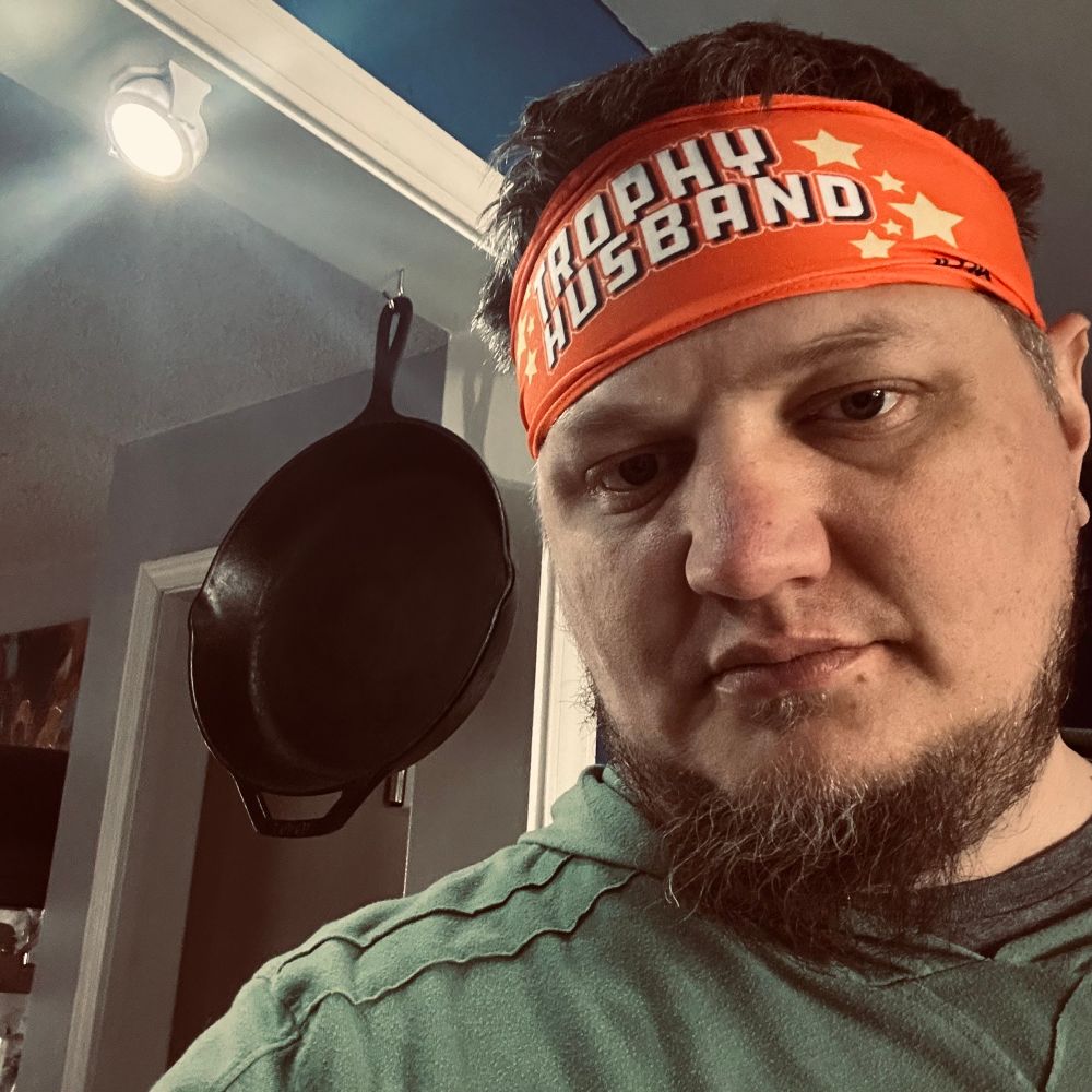 selfie of man wearing orange sweatband, cast iron pan hanging behind him