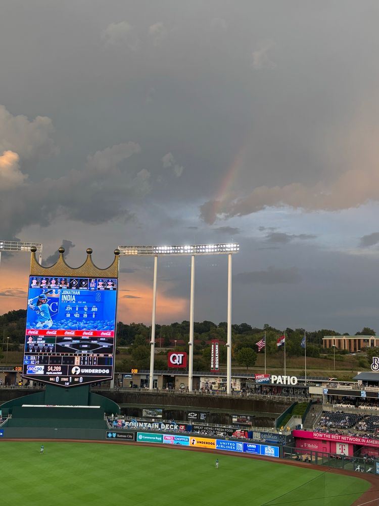 Cloudy sky with rainbow through the clouds over  the outfield and scoreboard  at Kauffman Stadium. 