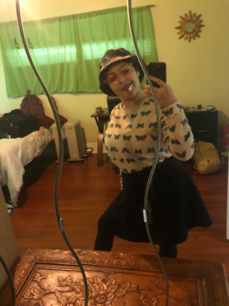 Me posing with bucket hat glasses pen in mouth in front of a mirror 