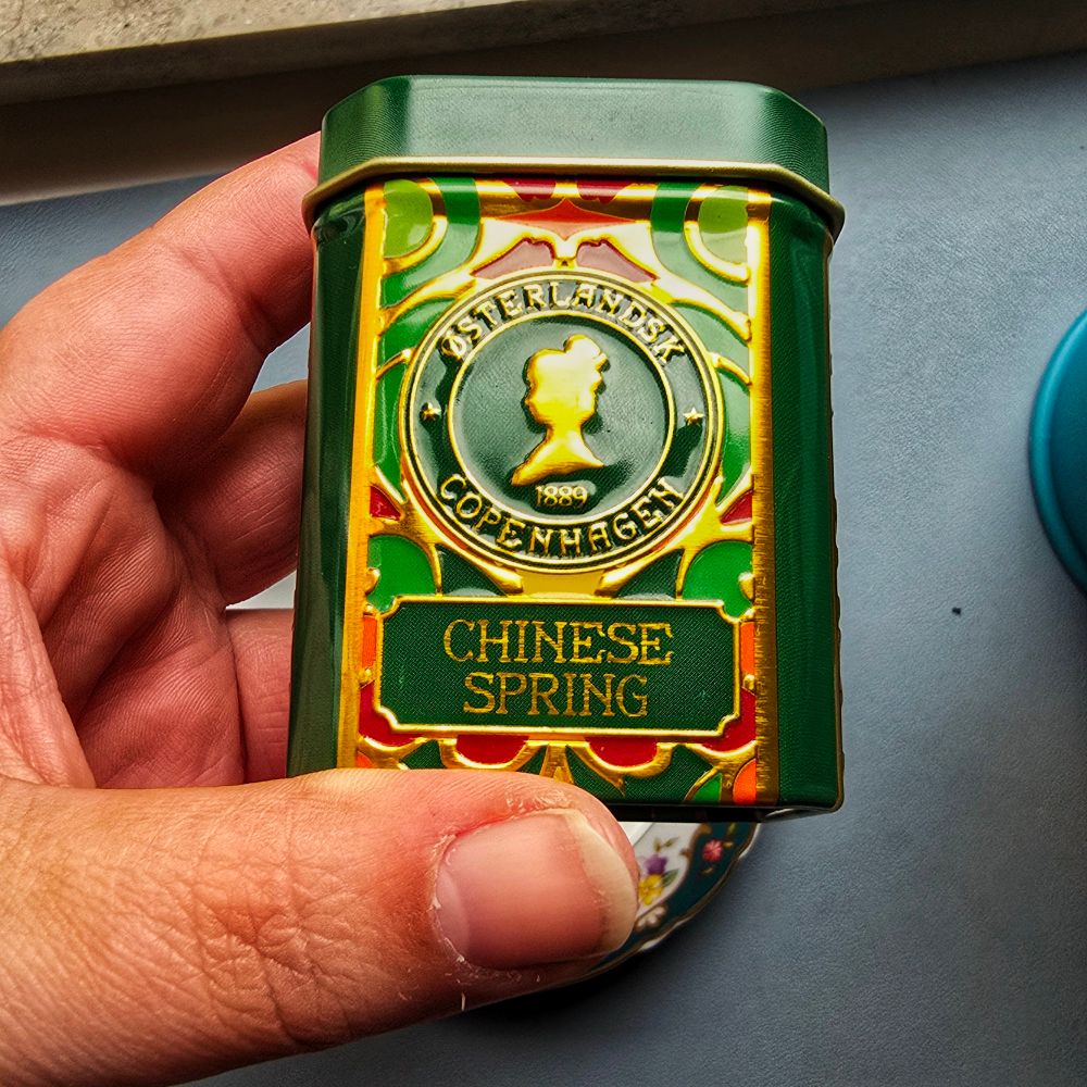 Photo of a hand holding a small colourful can. The can reads Østerlands Copenhagem 1889 - Chinese Spring.
