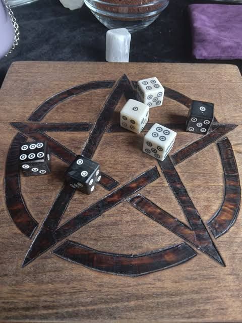 Seis dados de seis, 3 pretos e 3 brancos, lados rolados sobre uma tábua de madeira com um pentagrama incrustado
