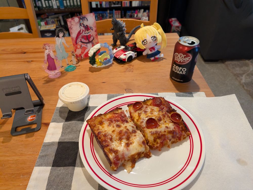 2 slices of Detroit Style pizza, one with cheese only and one with cup pepperoni, a side of ranch for dipping, and Dr Pepper Zero to drink, in the background, various anime acrylic Love Live stand-ups, Pokemon figures, Godzilla figure, Nijika plushie, a Lego Porsche Hypercar, and Yuki Setsuna preside