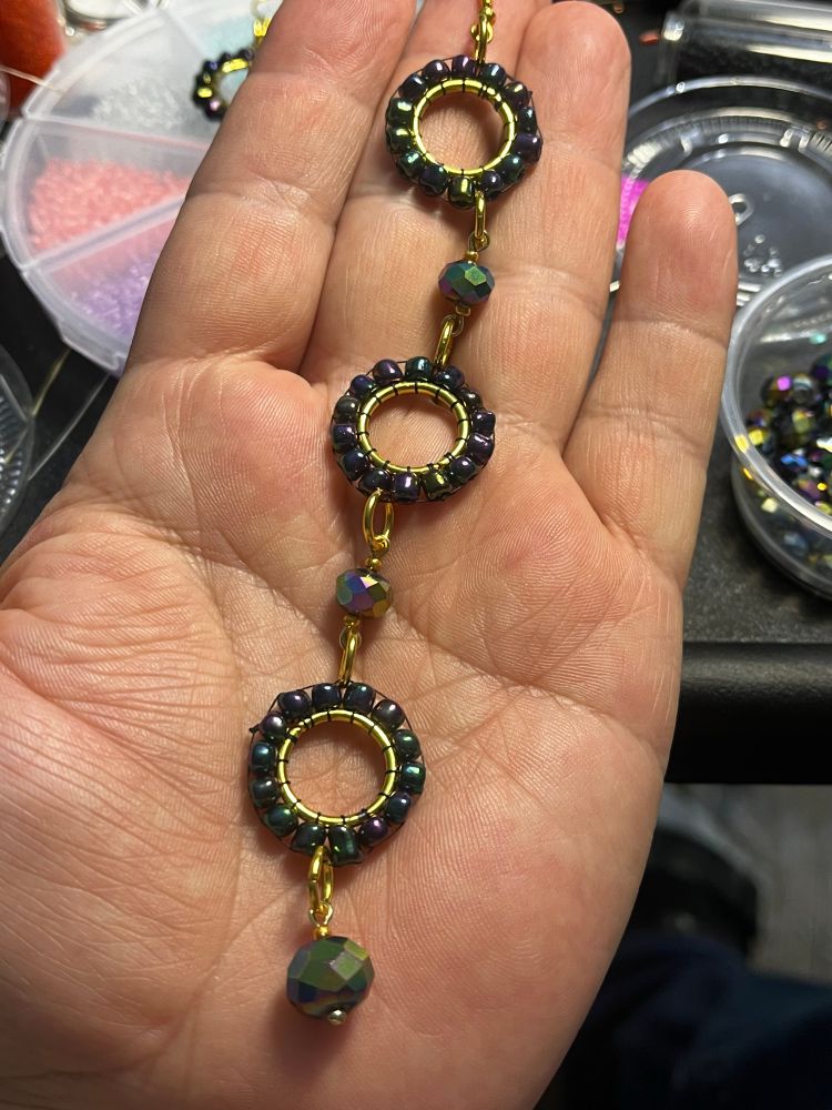 A beaded earring in my hand there are three gold circles with beads all around them and connected into them between them are facetted glass beads