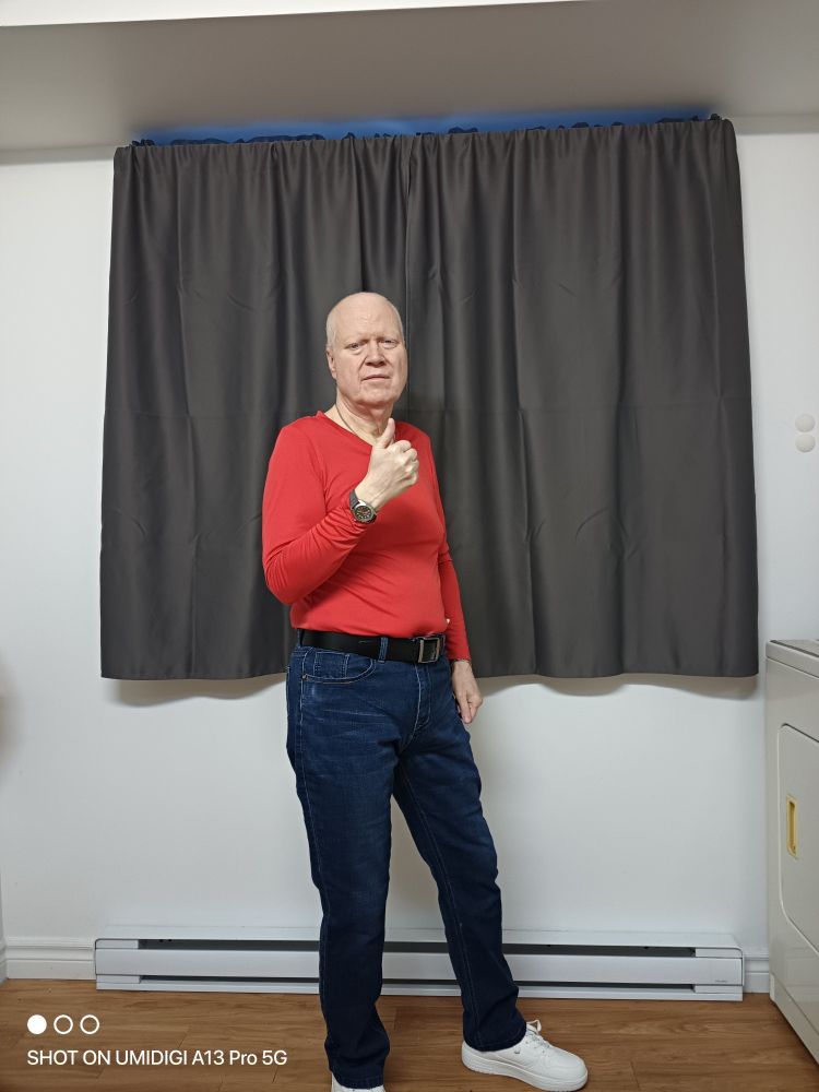 62 year old me, wearing white runners, Blue jeans, a red v-neck and thumb up 