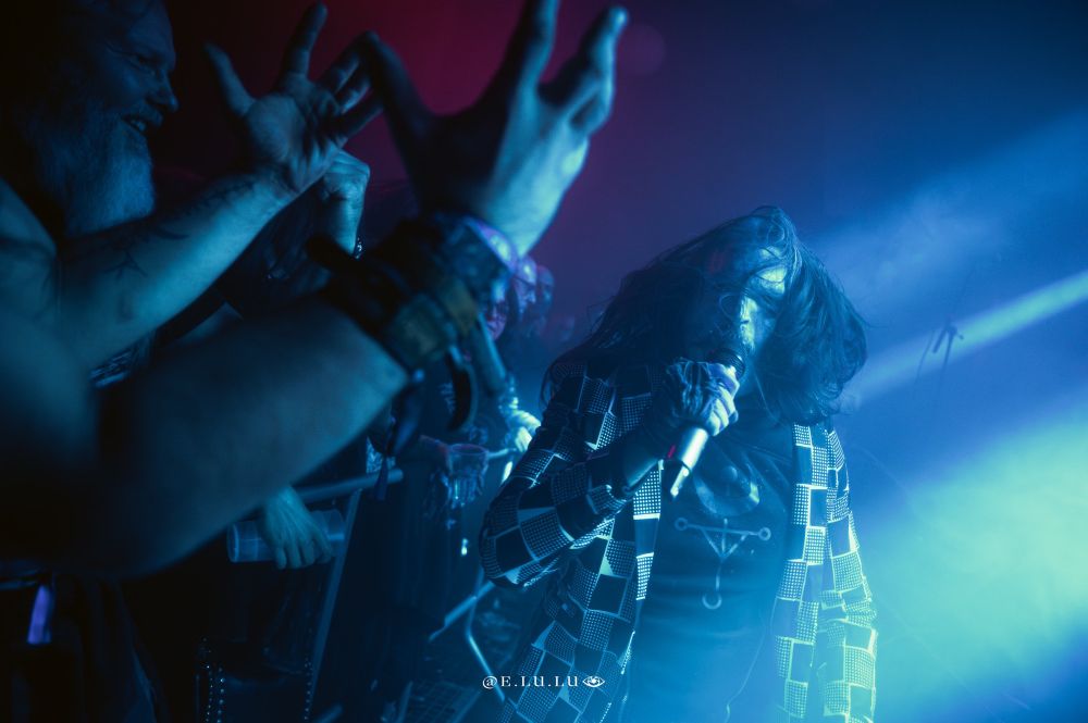 In a playful moment, Vicotnik of Dødheimsgard has stepped down into the photo pit to interact with fans, their hands reaching eagerly toward him as he leans in with a spirited attitude.