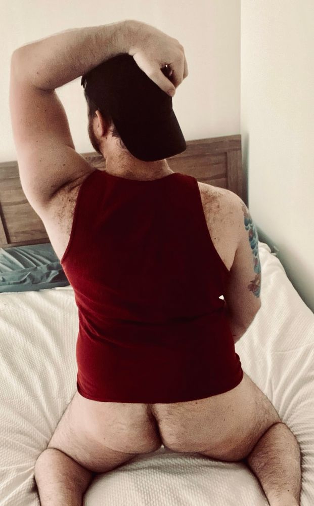 me kneeling on a bed facing away with a red tanktop and ass out
