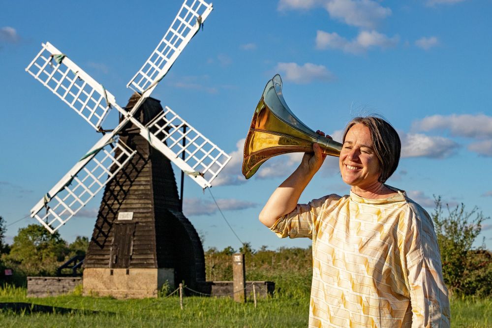 a woman listens to a golden horn next to the windmill