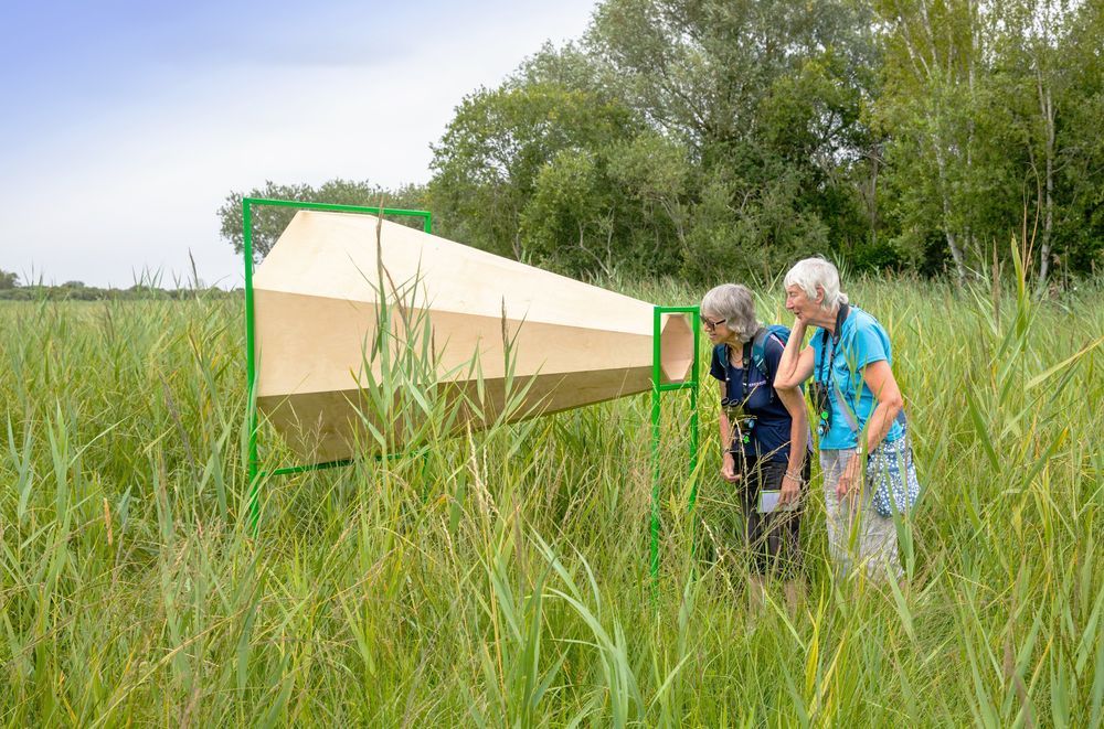 two woman listen to a giant listening horn on the fen