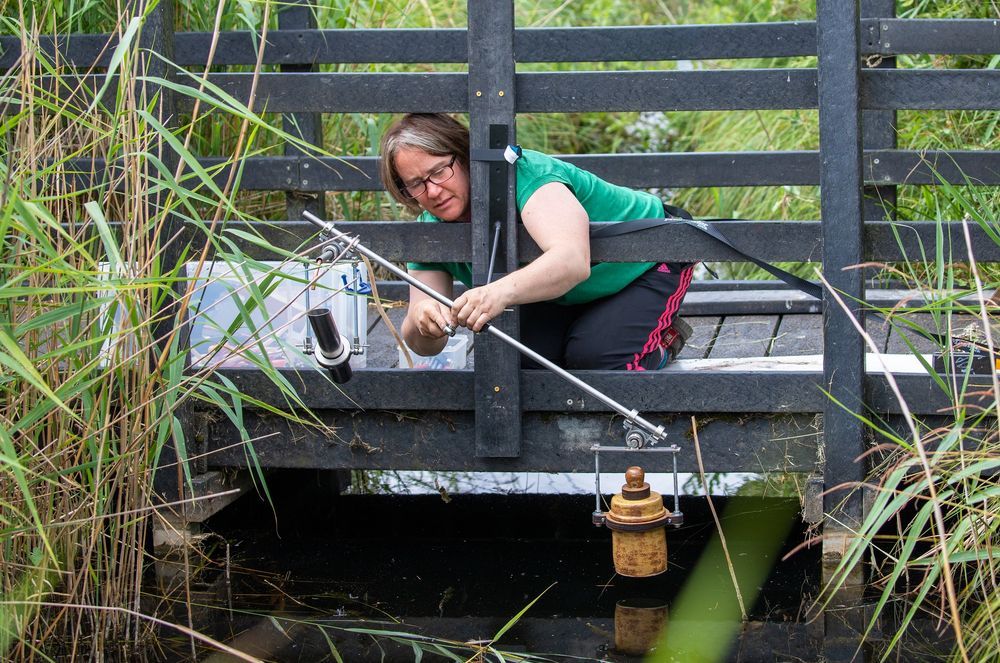 a woman attaches a listening device to a bridge over the river