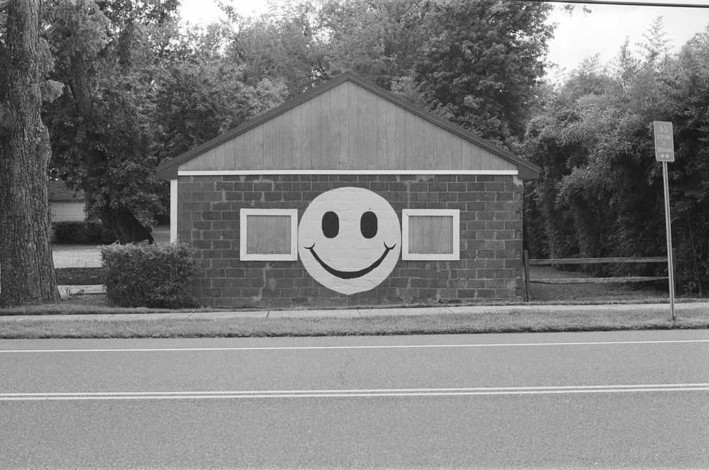 Picture of a small building from the road side with a large smiley face painted on its side. 