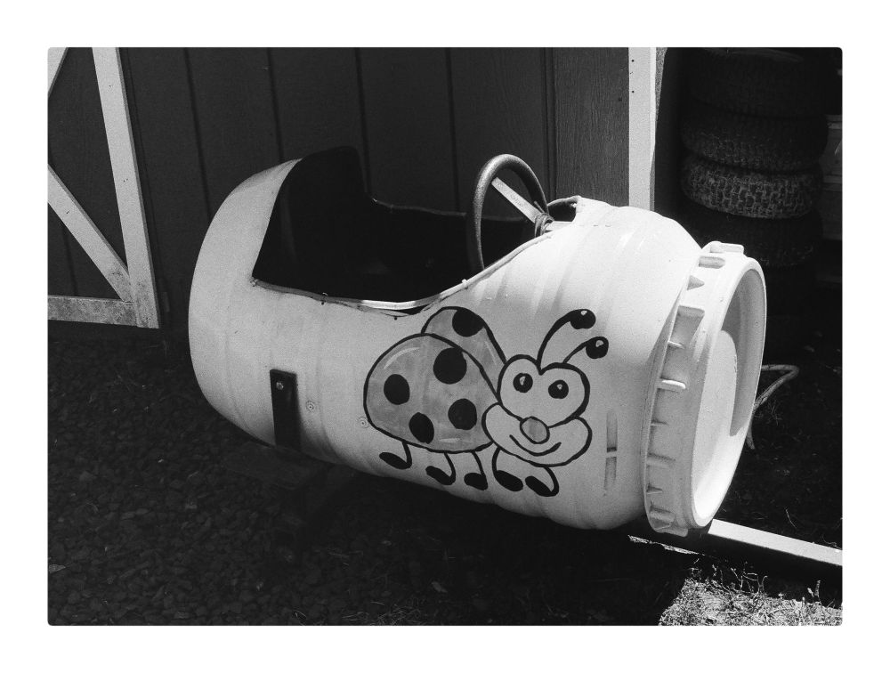 Children’s tractor train car made from a large screw lid storage barrel, painted white with a cutout for the seat and steering wheel that has a funny ladybug painted on its side with a friendly smile. 