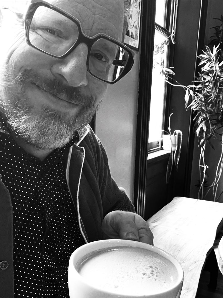 B&W photo of Andrew holding a mug of chai in a coffee shop ☕️ 