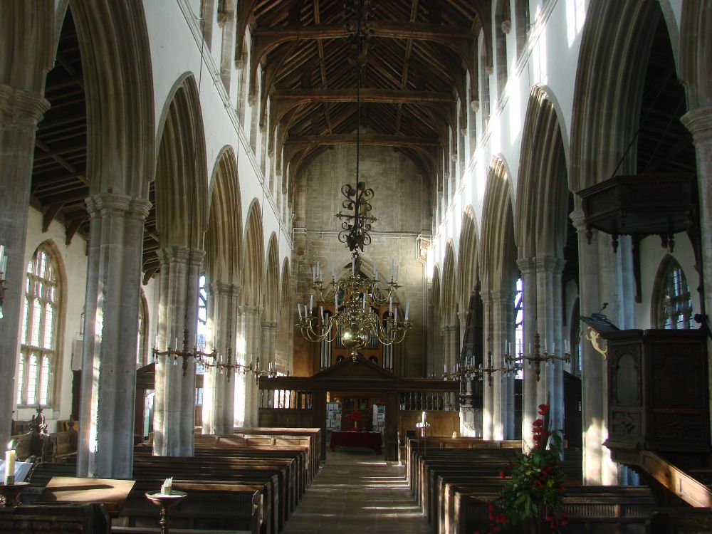 Looking west down the arcaded nave of a large late-medieval parish church with sunlight streaming through the south aisle windows.