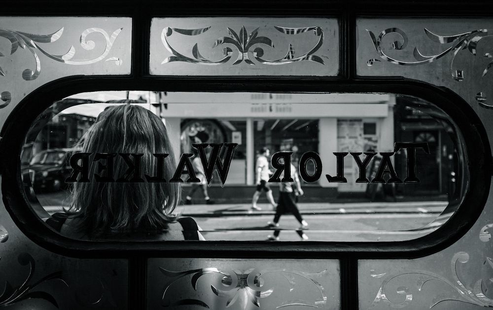 A monochrome street scene in Soho, London through the window from inside a pub. Taken with the Fuji X-T3 + 14mm f/2.8 lens.
