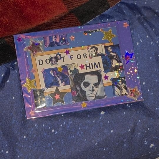 An edited image from the simpsons of homer's desk, sign that says 'do it for him' with photos of papa three layered on it. It has been laid over a pink iridescent frame with star stickers and a holographic star film on top 