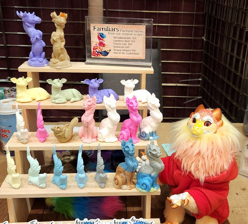 Peaches pointing at a tiered shelf of small resin sculptures. There are skull cats, salamanders, scugog dragons, a bird and ewenicorns.