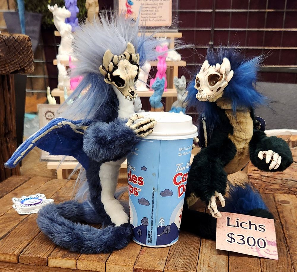 Two skull faced dragon art dolls examine a coffee. They seem....skeptical.