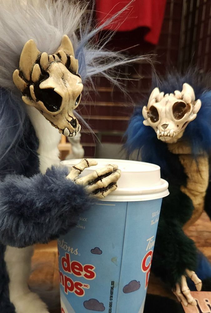 Two skull faced art dolls ponder a tim hortons coffee.