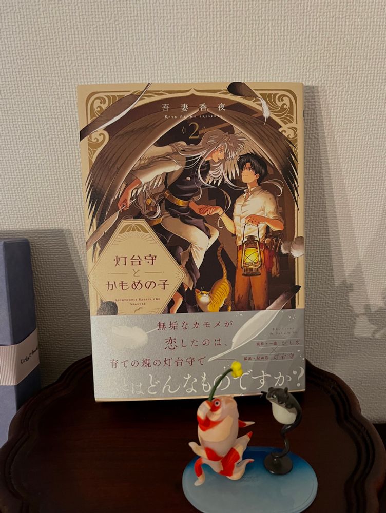 吾妻香夜先生の漫画『灯台守とかもめの子』2巻の書影。かもめの翼のある長髪の青年とカンテラを持った青年が手を繋いで見つめ合っている。