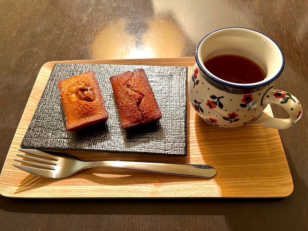 紅茶とフィナンシェのセット。中欧風の花柄のコップとフィナンシェの皿が木製のプレートに載っている。